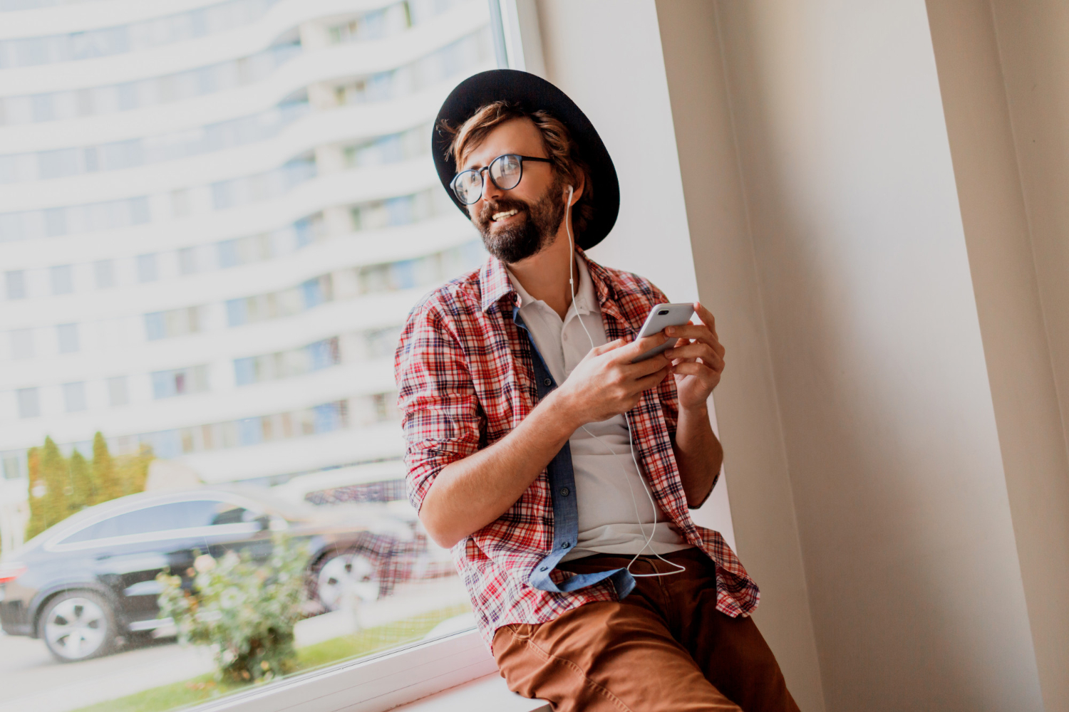 Man holding a mobile phone and looking out the window smiling